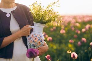 Hands of a young woman holding a jug with flowers in a field photo