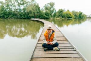 A teenage boy sits on a bridge on a pond and holds a poppy flower in his hands photo