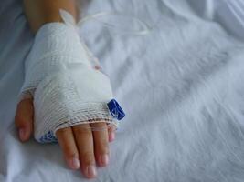 The patient's hand is wrapped in white bandages and has a saline line. photo
