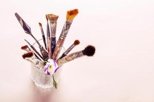 Art brushes and flowers in glass on table. Selective focus photo