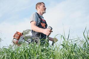 Man in overalls with weed trimmer mowing tall grass photo