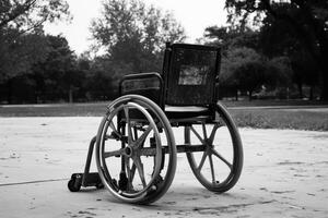An empty wheelchair sits on a paved pathway, surrounded by trees in an outdoor setting photo