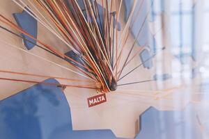 Abstract colored threads stretched on pins on map, depicting flight directions from Malta around World. Logistic grid, geometric, connections, isometrics and spirograph concept photo