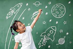 A young girl is pointing at a chalkboard with space and rocket drawings photo