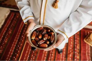 A man in a traditional outfit holds a bowl of dates photo