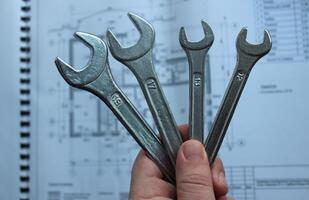 Human Hand Clenched Variety Spanners On Defocused Background Of Private House Interior Diagram With Technical Data photo