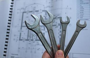 Engineer Holds Bunch Of Wrenches Over Blurred Paper Blueprints Of House Internal Walls And Construction Parameters photo