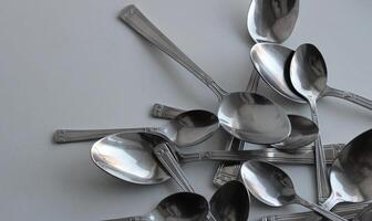 Big And Small Metallic Spoons Scattered On White At A Side Of Image With Clean Part For Title Or Logo. Dishware Concept Design Stock Photo