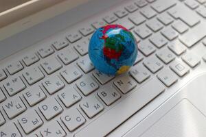North and South America continents mapped on a globe model lying on a laptop keypad with latin and cyrillic letters photo