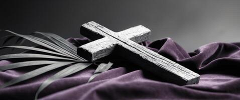 Wooden cross with palm leaf on the background of a purple cloth. photo