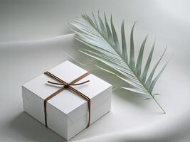 Simple White Square Box Tied with Brown Twine on Gray Surface with Palm Leaf. photo