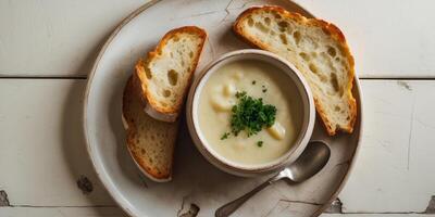 A bowl of soup with bread and a spoon on a white plate photo