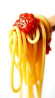 Twisted spaghetti strands topped with bright tomato sauce on a wooden fork photo