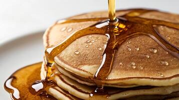 Closeup view of fluffy pancakes with syrup drizzling over the top on a plain plate photo