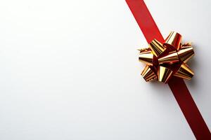A festive image featuring a gold gift bow resting on a smooth, white surface with a bold red ribbon accent. Ideal for holiday promotions, celebrations, or gift-related themes. photo