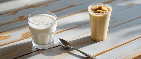 A glass of milk and a spoon next to a peanut butter smoothie photo