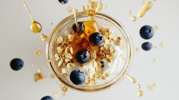 Deliciously messy parfait with yogurt, blueberries, granola, and honey drizzling from above photo
