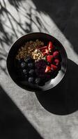 Bowl filled with mixed berries, granola, and almond flakes on a textured surface in natural light photo