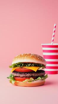 Perfectly symmetrical mega hamburger with vibrant colors and a striped cup on a pink backdrop photo