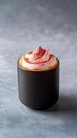 Rich turmeric-infused hot beverage topped with whipped cream sits in a black mug on a textured gray surface photo