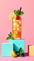 Iced tea in a modern curved glass with ice, mint, and lemon sits on colorful geometric blocks against a pink background photo