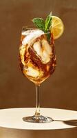 Refreshing beverage served in a stylish glass with ice, lemon, and mint on a curved surface against a warm backdrop photo