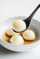 Minimalist white bowl filled with smooth glossy dumplings in light broth on a plain surface photo