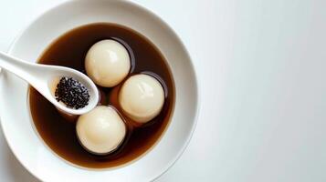 Minimalist white bowl filled with smooth glossy dumplings sitting in dark syrup on a clean surface photo