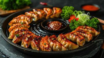 Sizzling pan of golden-crisp gyoza arranged with fresh vegetables and dipping sauces photo