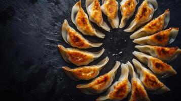 Modern presentation of pan-seared dumplings arranged in a circular pattern on a dark surface photo