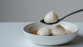 Delicate glossy dumplings in a minimalist white bowl with a spoon drizzling sauce photo