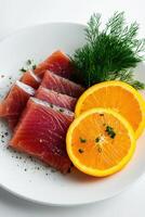 Tuna sashimi with fresh orange slices garnished with herbs served on a white plate for a healthy meal option photo