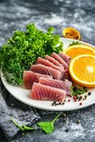 Freshly prepared tuna sashimi with orange slices and greens on a white plate, garnished with spices photo