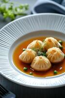 Delicate soup served in a white plate with beautifully arranged dumplings garnished with herbs and peas photo