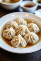 Delicately arranged soup dumplings served in flavorful broth on a white plate at a cozy dining setting photo