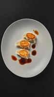 Dumplings served with soy sauce on a sleek white plate against a dark background photo