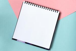 Mock up of scketchbook on pastel pink and blue background. Top view of open notebook with clean sheet. Template for message. Copy space. photo
