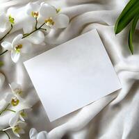 Elegant white blank card for wedding invitation mockup surrounded by delicate white orchids on soft beige fabric conveys a sense of calm and simplicity suitable for various occasions and messages photo