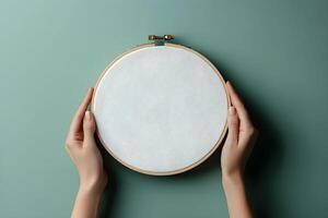 Hands holding an empty embroidery hoop for mockup on a green background, preparing for a new crafting project photo