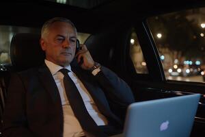 A man in a suit and tie sitting in the back seat of a car on the phone photo