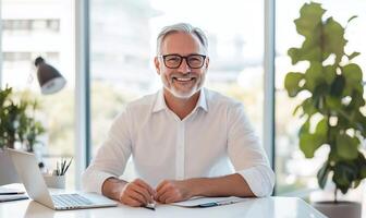Smiling mature man sits at a desk in an office, happy and professional. photo