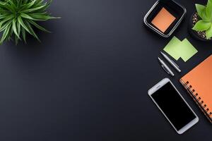 Dark gray office desk workspace with plants, sticky notes, pen, notebook, and smartphone. photo