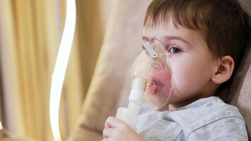 Child using a nebulizer in a calm room. Young boy is receiving treatment with a nebulizer while relaxing in a softly lit room, showing focus and resilience. video