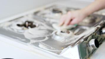 Cleaning a kitchen stove with soap foam. A person scrubs a kitchen stove covered in soap foam, focusing on removing grease and grime effectively. video