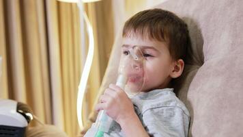 Boy with nebulizer for breathing. A young boy rests in bed while using a nebulizer to assist with breathing. The room has soft lighting. video