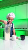 Child makes a recipe in a bright kitchen. A young child in a chef hat stirs ingredients in a blender while preparing a meal in a modern kitchen setting. video