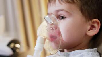 Boy using nebulizer for breathing. A young boy is seated indoors, focusing on using a nebulizer to help with his breathing. video