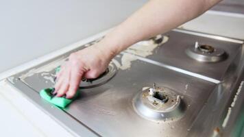 Cleaning stove top with elbow grease. A hand wipes down a greasy stove top using a green cloth, removing food residue and ensuring cleanliness. video