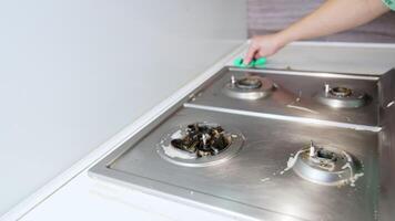 Cleaning a stovetop in a modern kitchen. A person scrubs a stovetop to remove burnt residue and grease, ensuring a tidy and hygienic cooking space. video