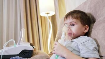 Boy using nebulizer for asthma. A young boy is sitting comfortably at home using a nebulizer for his asthma treatment, wearing a mask. video